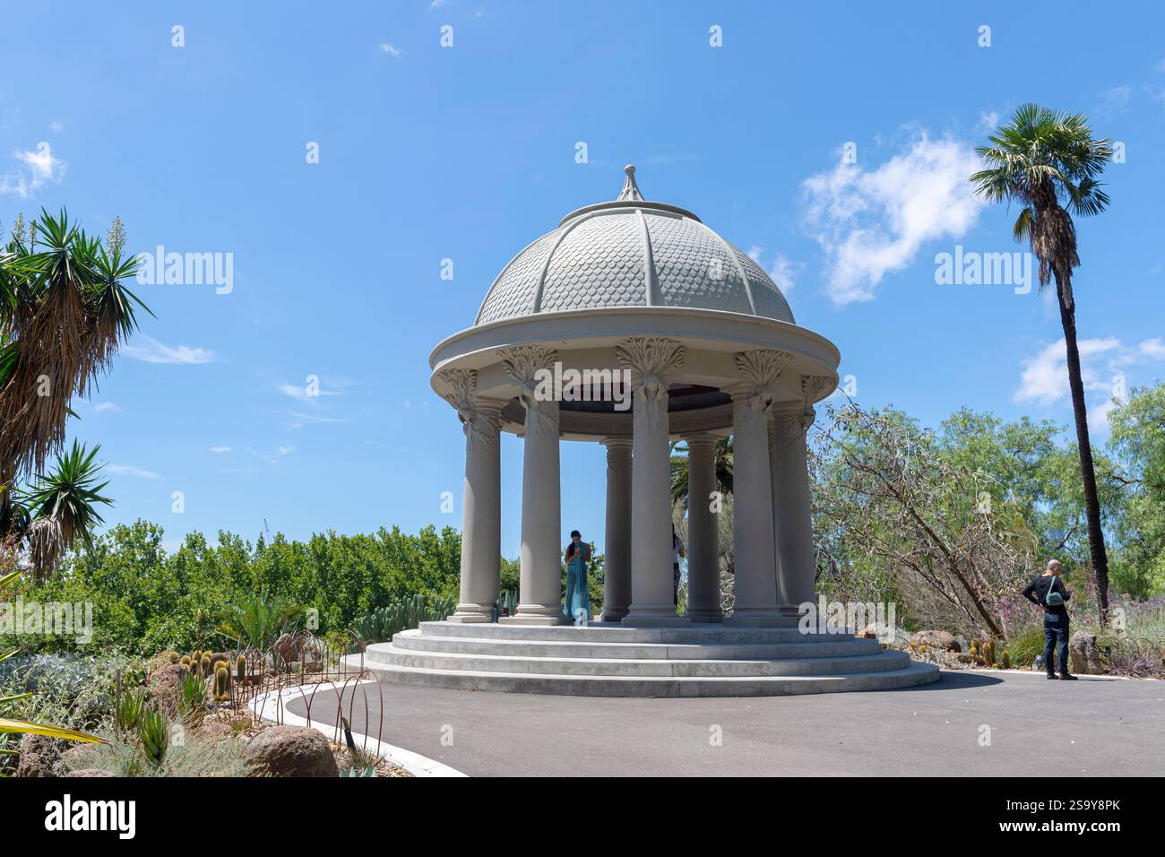 Asiatisches Mädchen in blauem Kleid, hinterleuchtet von der Sonne, macht Selfie zwischen klassischen Säulen The Temple of the Wind, Royal Botanic Gardens, Melbourne, Australien Stockfoto