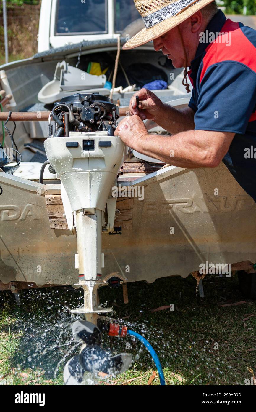Mann führt Wartung Außenbordmotor kleine Bootsszene demonstriert Handarbeit Reparatur Outdoor Aktivität Wasser Spritzen von Propeller Strohhut Stockfoto