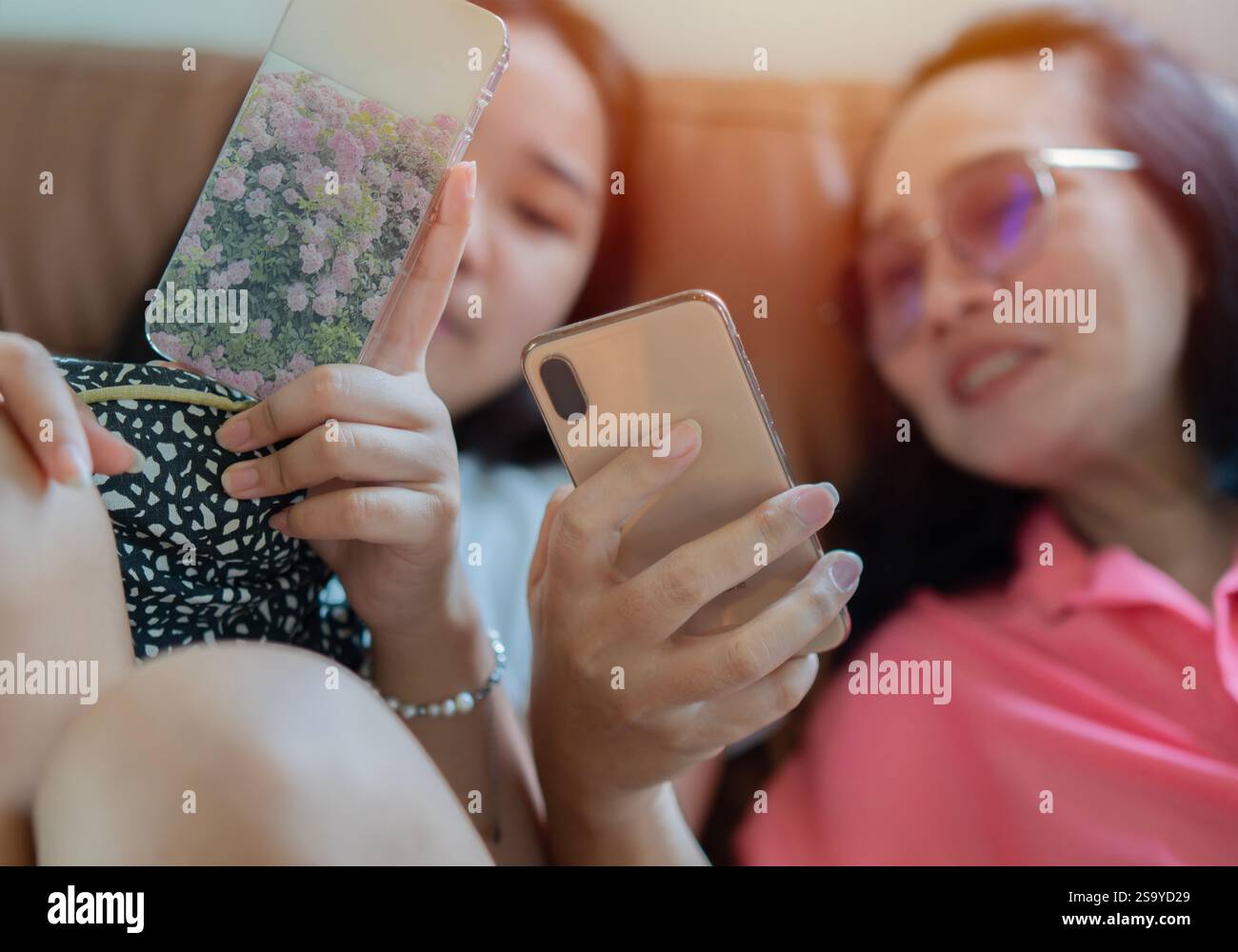 Zwei junge Erwachsene Freunde lachen zusammen und nutzen ihre Smartphones zu Hause online. Selektiver Fokus auf die Hände. Stockfoto