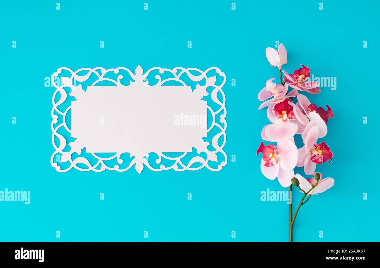 Schöne Orchideenblume auf hellblauem Hintergrund mit Papierkartennotiz. Minimales Konzept. Kreatives Layout für Frühling und Sommer. Blumenästhetik. Stockfoto