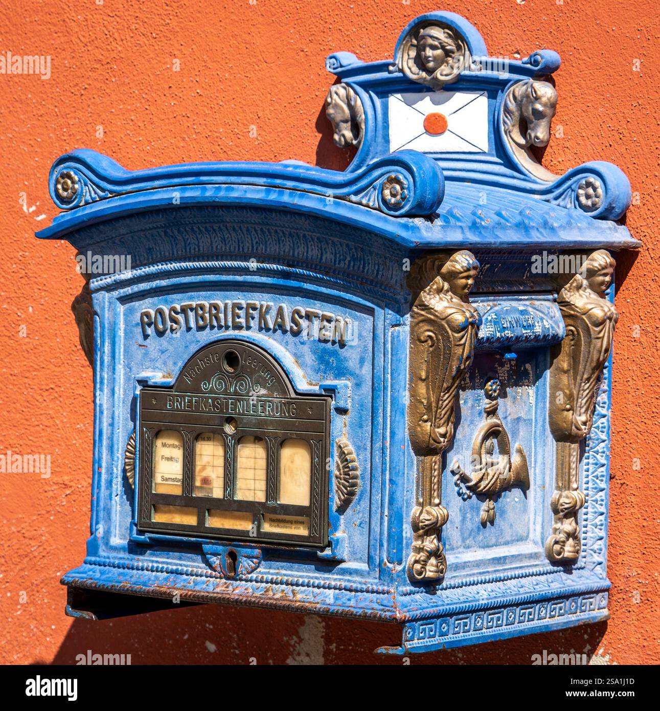 Ein an der Wand montierter, blauer Briefkasten mit verzierten Dekorationen und einem Glasfenster zum Sammeln von Postsendungen. Die Mailbox ist sehr kompliziert Stockfoto