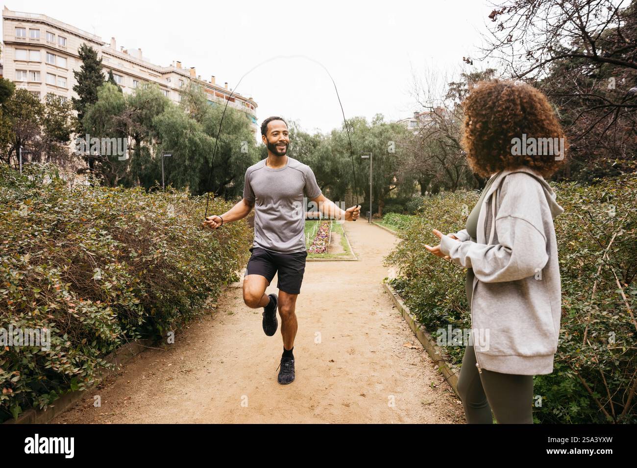 Ein Trainer führt eine Seilspringen-Übung in einem Park durch, während seine Kundin zusieht. Stockfoto