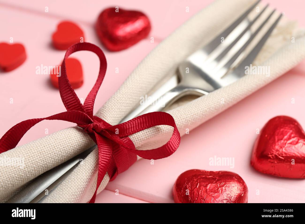 Romantischer Ort für den Valentinstag. Besteck, Serviette und dekorative Herzen auf rosafarbenem Holztisch, Nahaufnahme Stockfoto