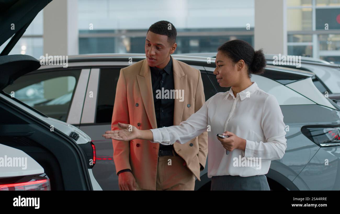 Afroamerikanische Frau Händlerverkäufer helfen Mann Kunde im Autohändlergeschäft Verkäuferin Consult zeigt automatische Kofferraumöffnungsfunktion von elektrisch Stockfoto