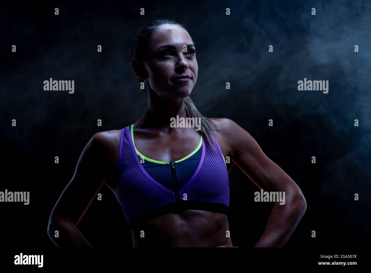 Eine entschlossene Frau in einem sportlichen Outfit steht in einem rauchigen Ambiente, verkörpert Kraft und Fitness und zeigt ihre inspirierende und befähigende A Stockfoto