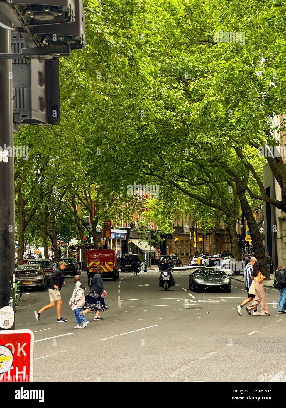 Belebte London Street mit Fußgängern und üppigen grünen Bäumen - Smartphone-aufgenommenes Stockfoto