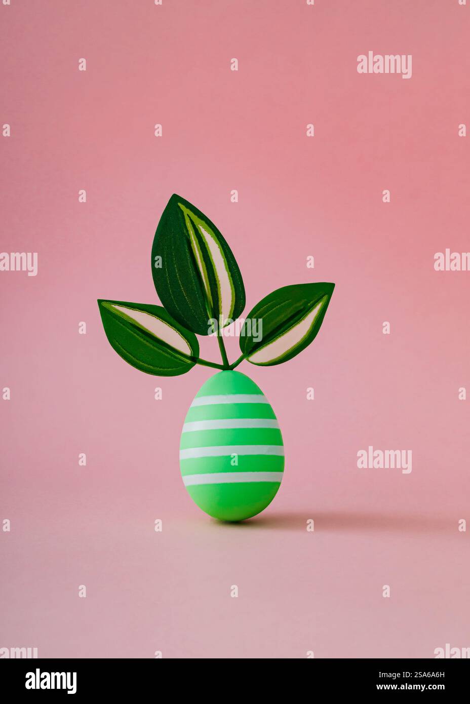 Grünes Osterei mit grünen Blättern auf rosa Hintergrund. Minimales Konzept. Kreatives, festliches Layout für Frühlingsferien. Osterästhetik. Stockfoto