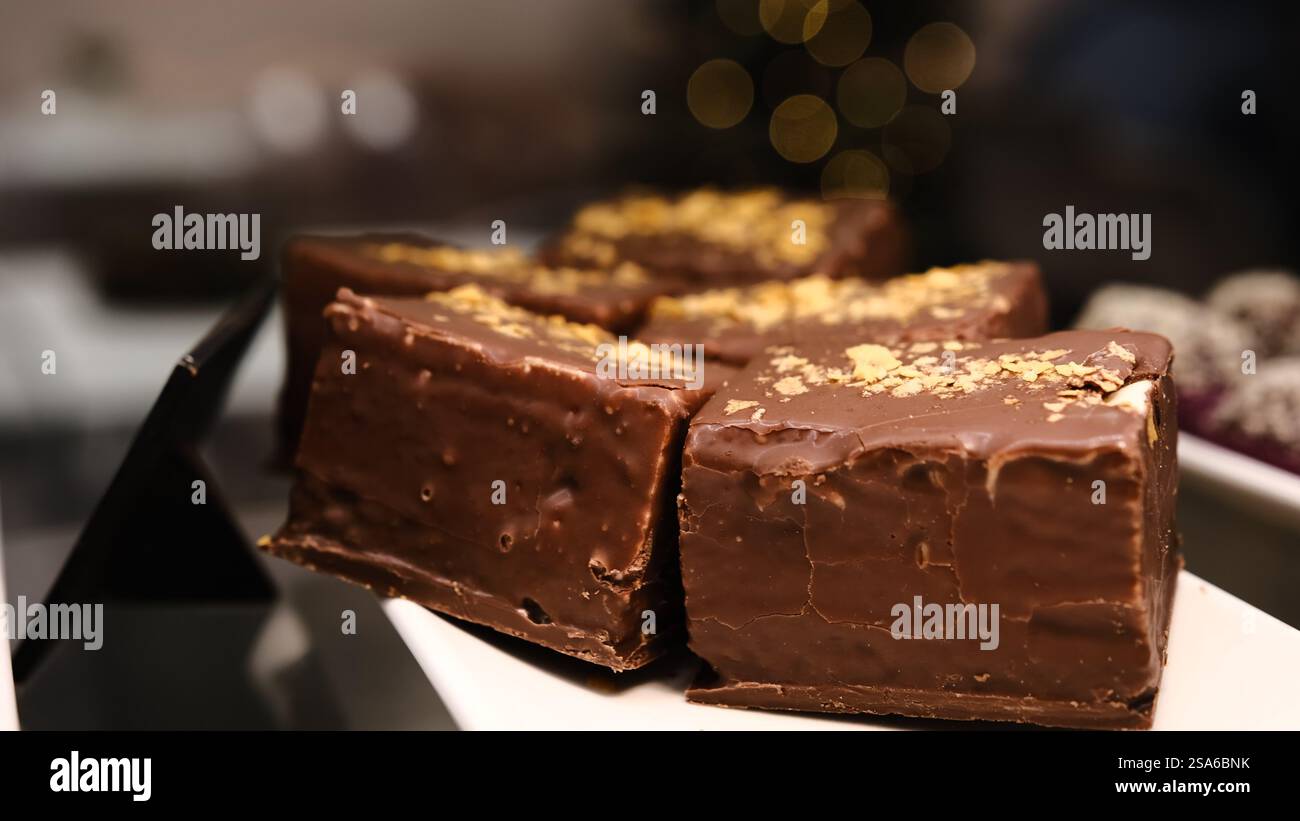 Große köstliche Vogelmilch Dessert Schokoladenüberzug gelbe Streusel weiße Teller angezeigt Theke verwöhnende süße Leckerei perfekt für Dessertliebhaber Stockfoto