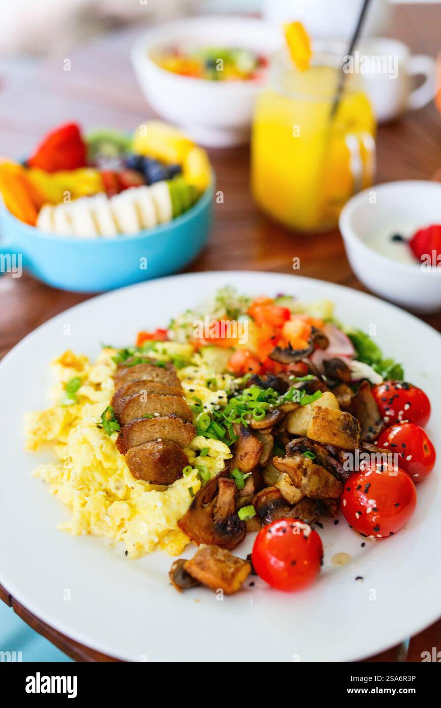 Vegetarisches Frühstück mit Rührei, Bratkartoffeln, Wurst auf Pflanzenbasis, sautierten Pilzen und Kirschtomaten Stockfoto