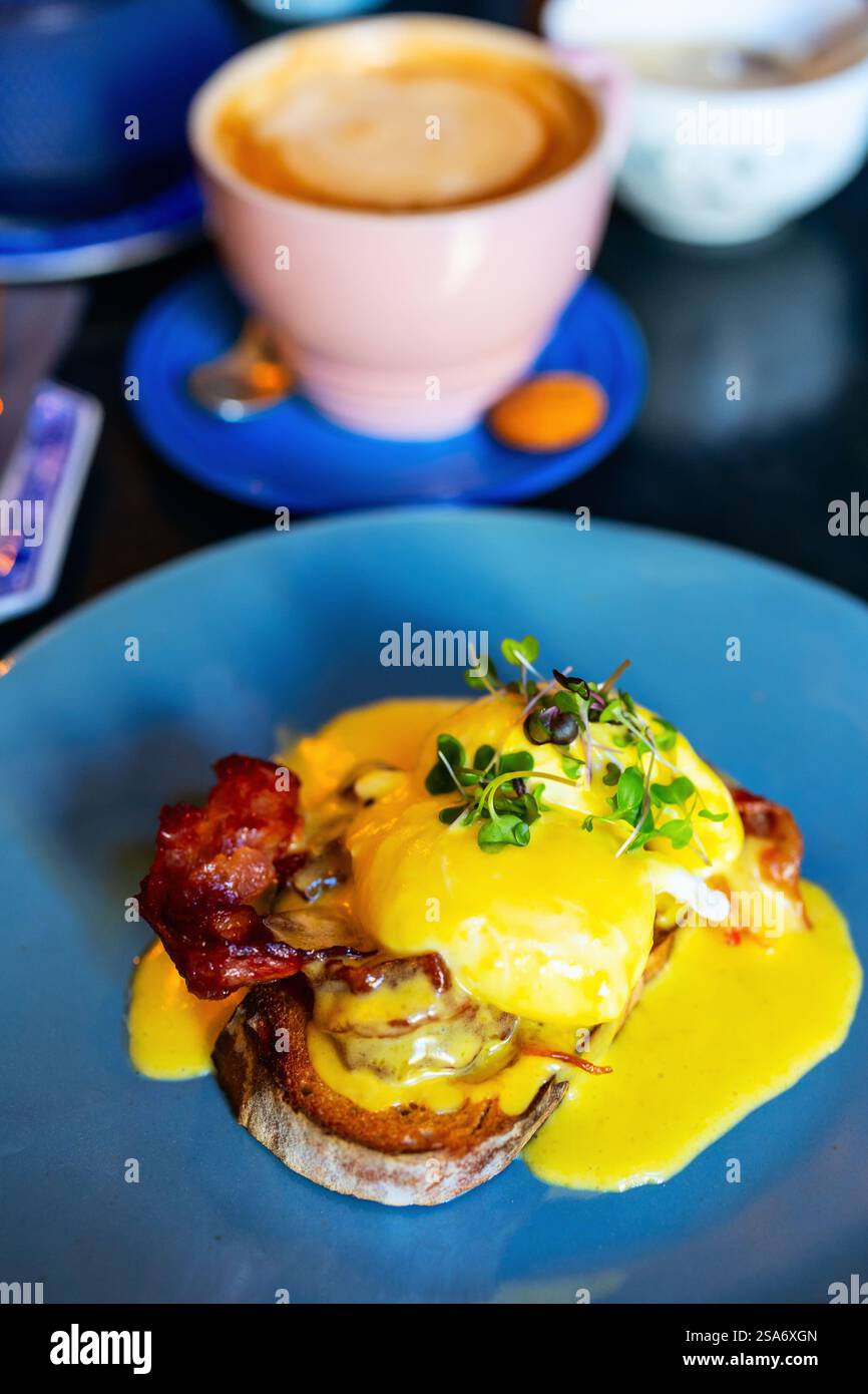 Klassisches Eggs Benedict mit pochierten Eiern, knusprigem Speck, Hollandaise-Sauce und MicroGreens-Beilage, serviert auf geröstetem Sauerteigbrot. Stockfoto