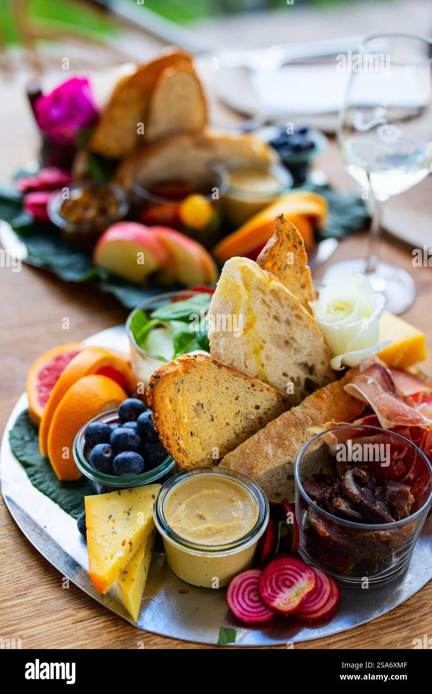 Eine lebendige Platte mit knusprigem Brot, verschiedenen Käsesorten, frischen Fruchtscheiben, Wurstwaren und cremigem Hummus, garniert mit bunten Rüben sl Stockfoto