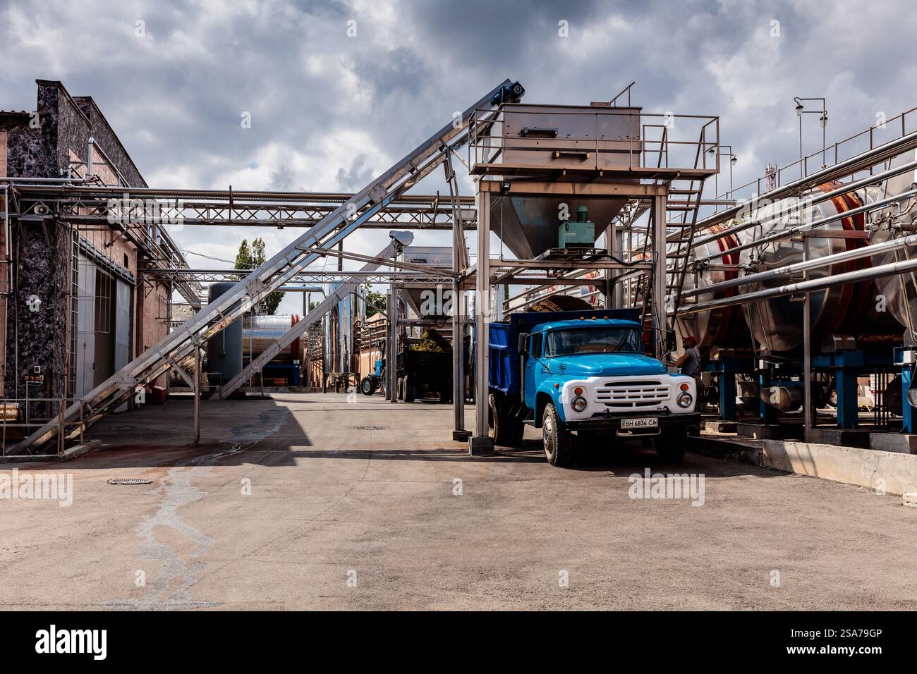 Vor einem großen Gebäude steht ein blauer Lkw. Der Lkw ist von vielen Rohren und einem großen Kran umgeben. Die Szene ist industriell und die Stimmung Stockfoto