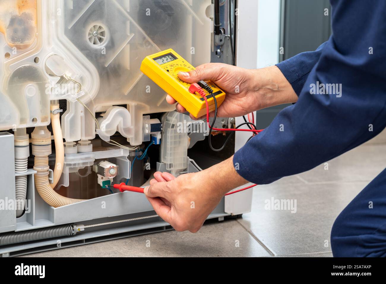 Schuss eines jungen Mannes, der ein elektronisches Multimeter benutzt, während er einen Geschirrspüler in einem Haus repariert Stockfoto