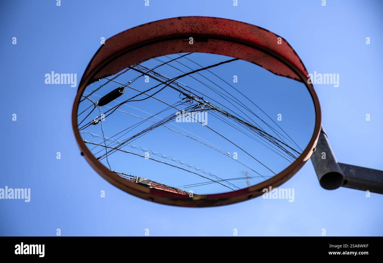 Blick auf einen runden, konvexen Straßenspiegel, der einen blauen Himmel und erhöhte Stromleitungen an einem klaren Tag im Westen Tokios reflektiert Stockfoto