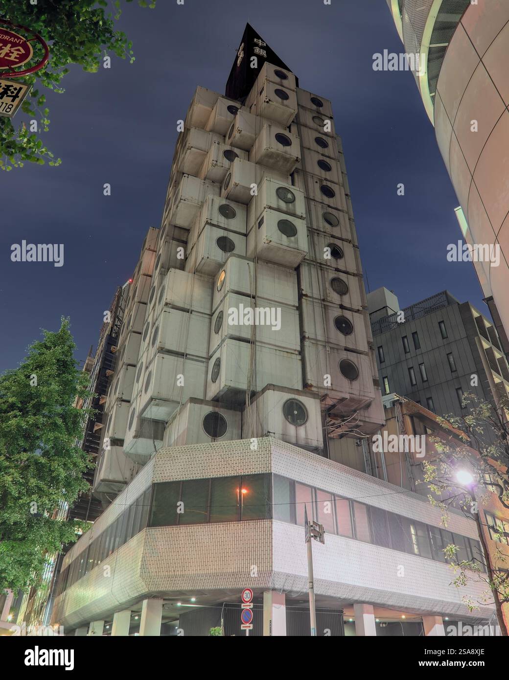 Nachtansicht mit Blick auf das Nakagin Capsule Tower Building von seiner Basis unter einem bewölkten Himmel Stockfoto