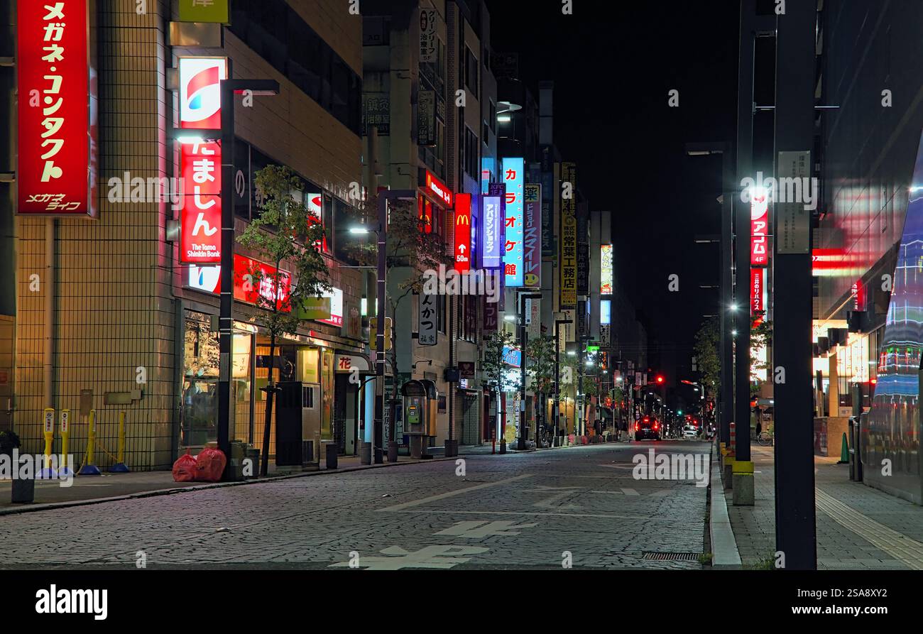 Spätabends Blick auf eine meist leere Straße in der Nähe des Mitaka-Bahnhofs im Westen von Tokio, beleuchtet durch eine Reihe von Ladenschildern und Straßenlaternen Stockfoto