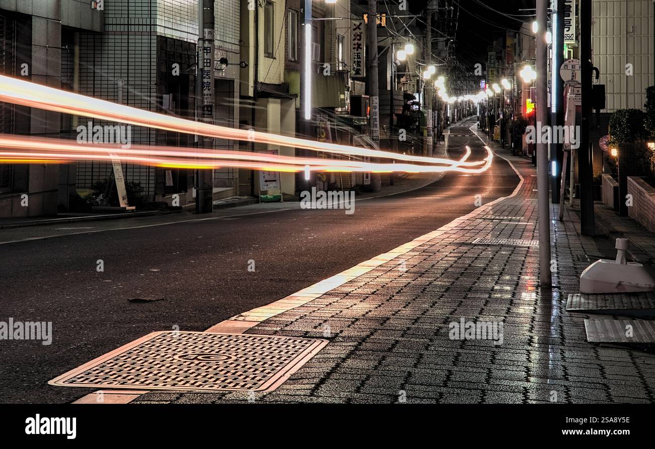 Nächtliche Sicht auf Lichtspuren, die durch eine lange Belichtung der Scheinwerfer eines Autos auf der Straße in Tokio, Japan, entstehen Stockfoto