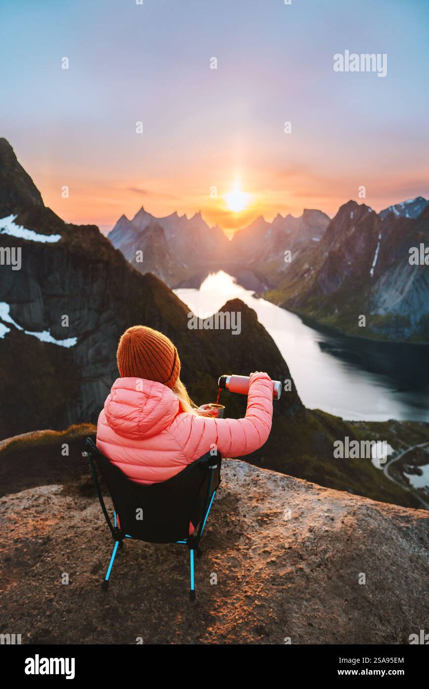 Frau trinkt Kaffee auf dem Berg Reinebringen, reist in Norwegen Wandern im Freien, Mädchen sitzt auf einem Campingstuhl und genießt Sonnenuntergang Lofoten Inseln Stockfoto