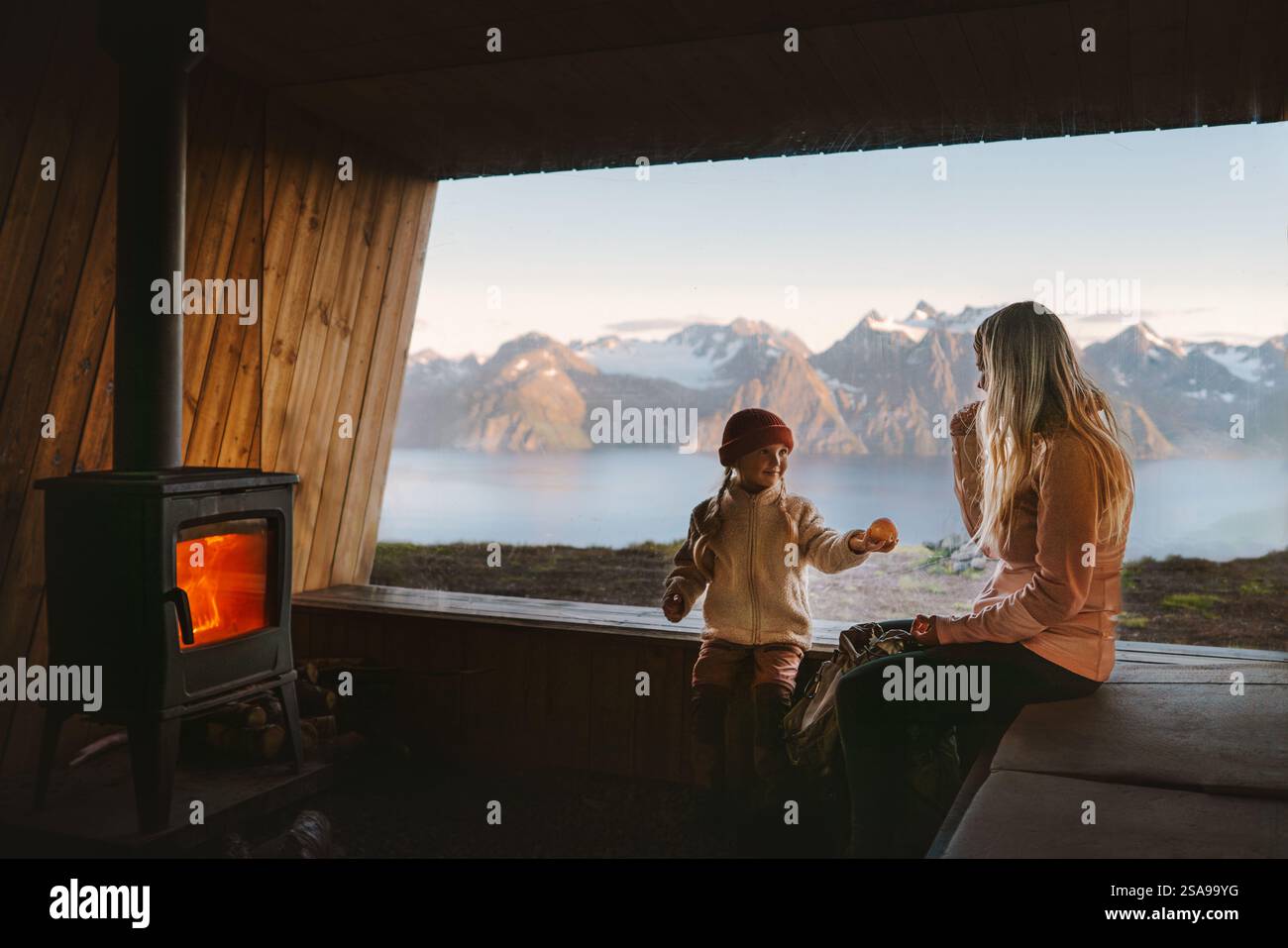 Familie Mutter und Kind entspannen in gemütlicher Berghütte mit Kamin und Panoramafenster mit Bergblick, Eltern reisen mit Kind in Norwegen A Stockfoto