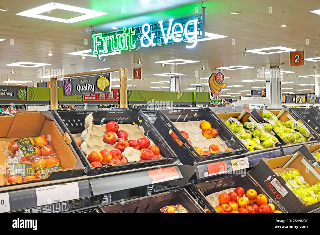 Ein Schild mit Obst- und Gemüsebeleuchtung an der Decke über Kunststoffkisten mit roten und grünen Äpfeln zum Verkauf oder Großpackungen Essex England UK Stockfoto