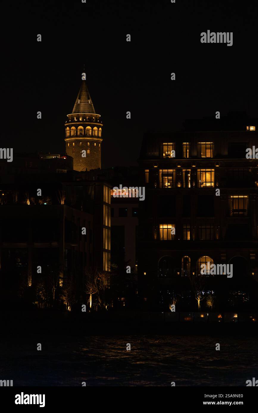 Nachtblick auf den beleuchteten Galatenturm und einen modernen Uhrenturm in Istanbul. Die warmen Lichter stehen im Kontrast zum dunklen Himmel Stockfoto