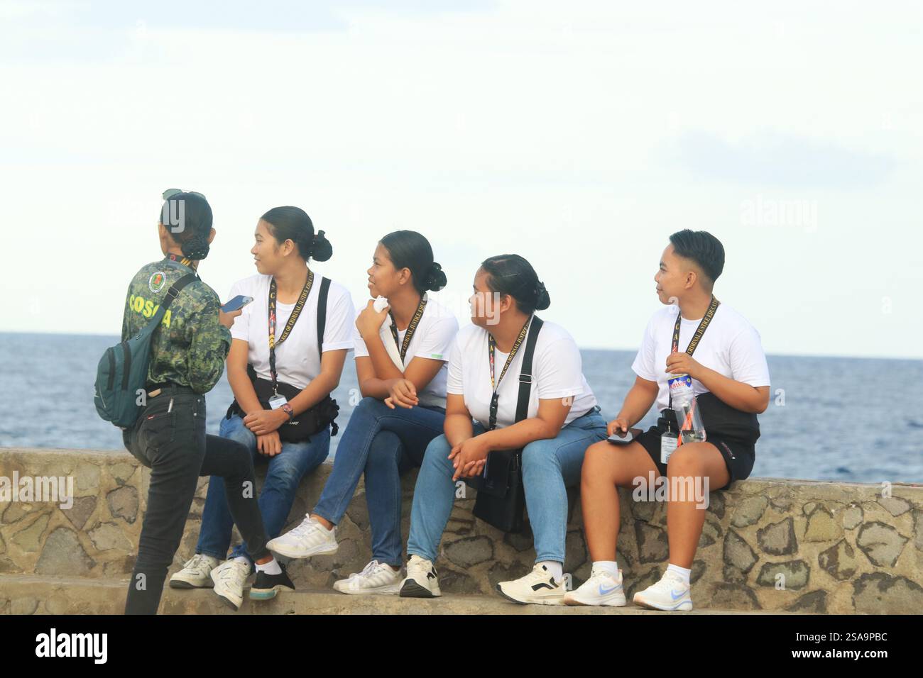 Dumaguete City, Negros Oriental, Philippinen - 25. Januar 2025: Eine Gruppe von Studenten sitzt am Rand der Meeresmauer des Pantawan Boulevard Stockfoto