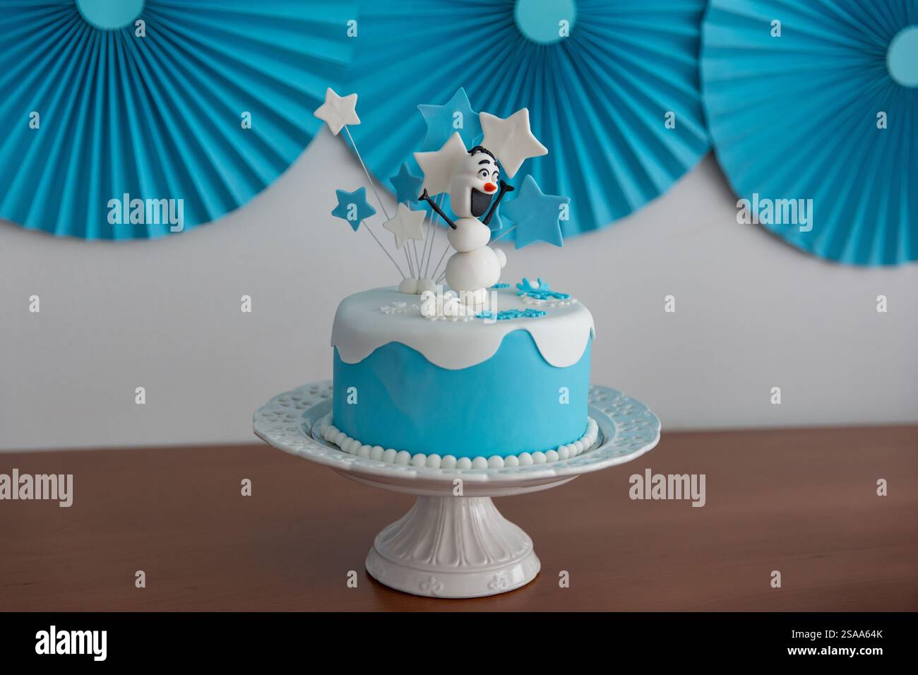 Geburtstagskuchen mit einem Schneemann und blauen und weißen Sternen auf dem Tisch Stockfoto