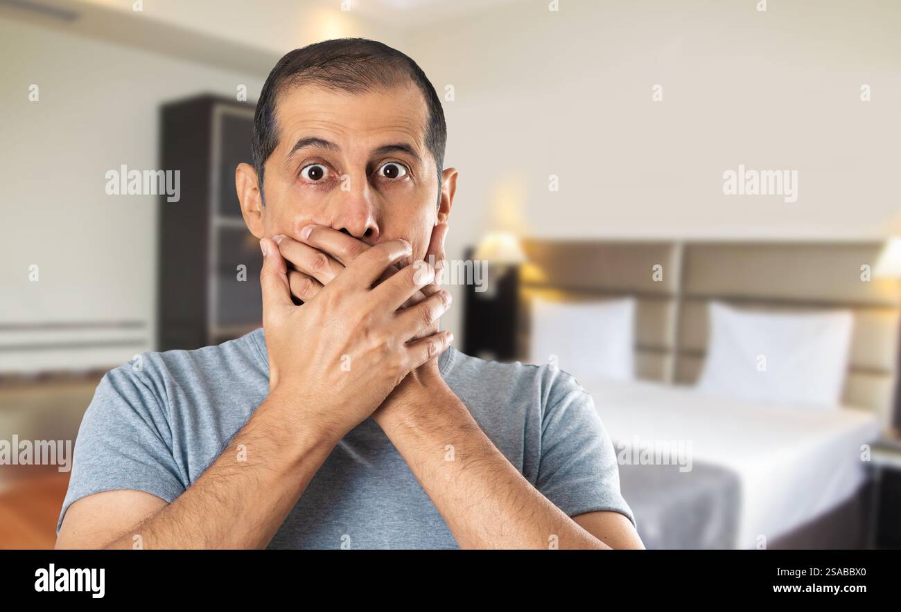 Schockierter Mann, der im Hotel seinen Mund mit Händen bedeckt Stockfoto