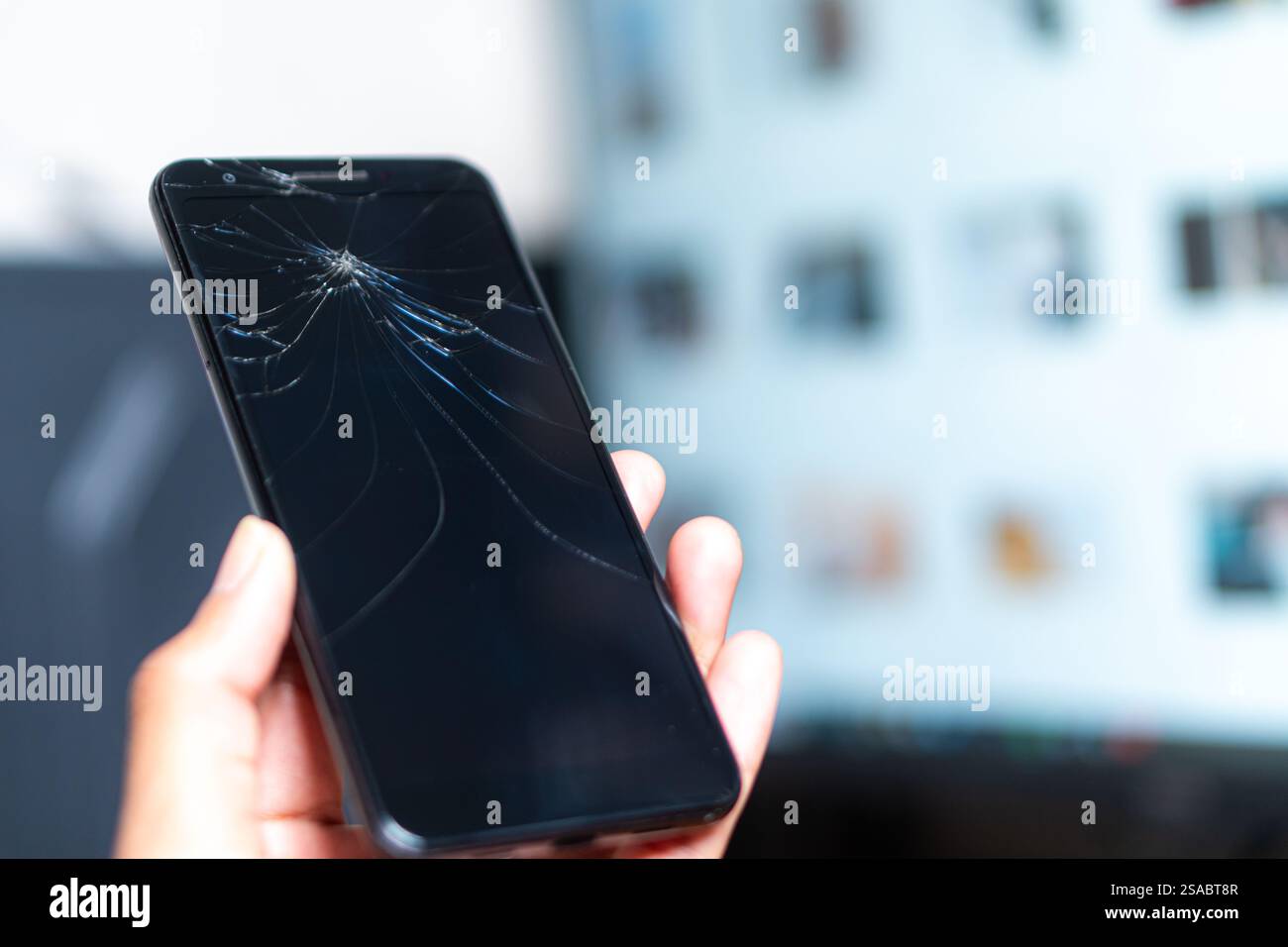 Eine Nahaufnahme einer Hand, die ein Smartphone hält, mit einem gerissenen Bildschirm vor einem weißen Hintergrund. Der Bildschirm ist dunkel und hebt das Spinnennetz hervor Stockfoto