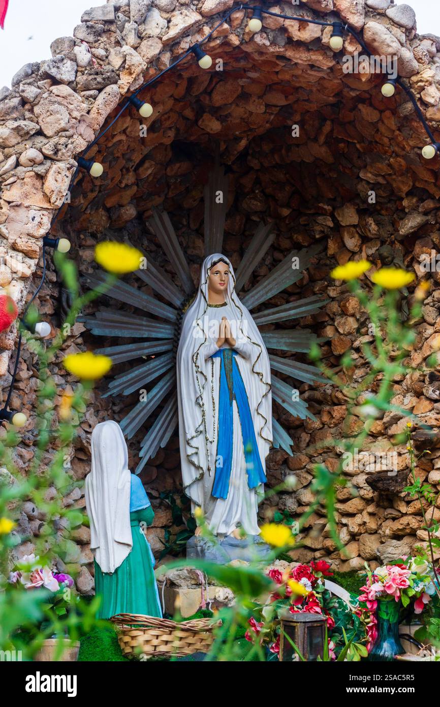 Marienstatue im religiösen Schrein im Freien mit Blumendekor Stockfoto