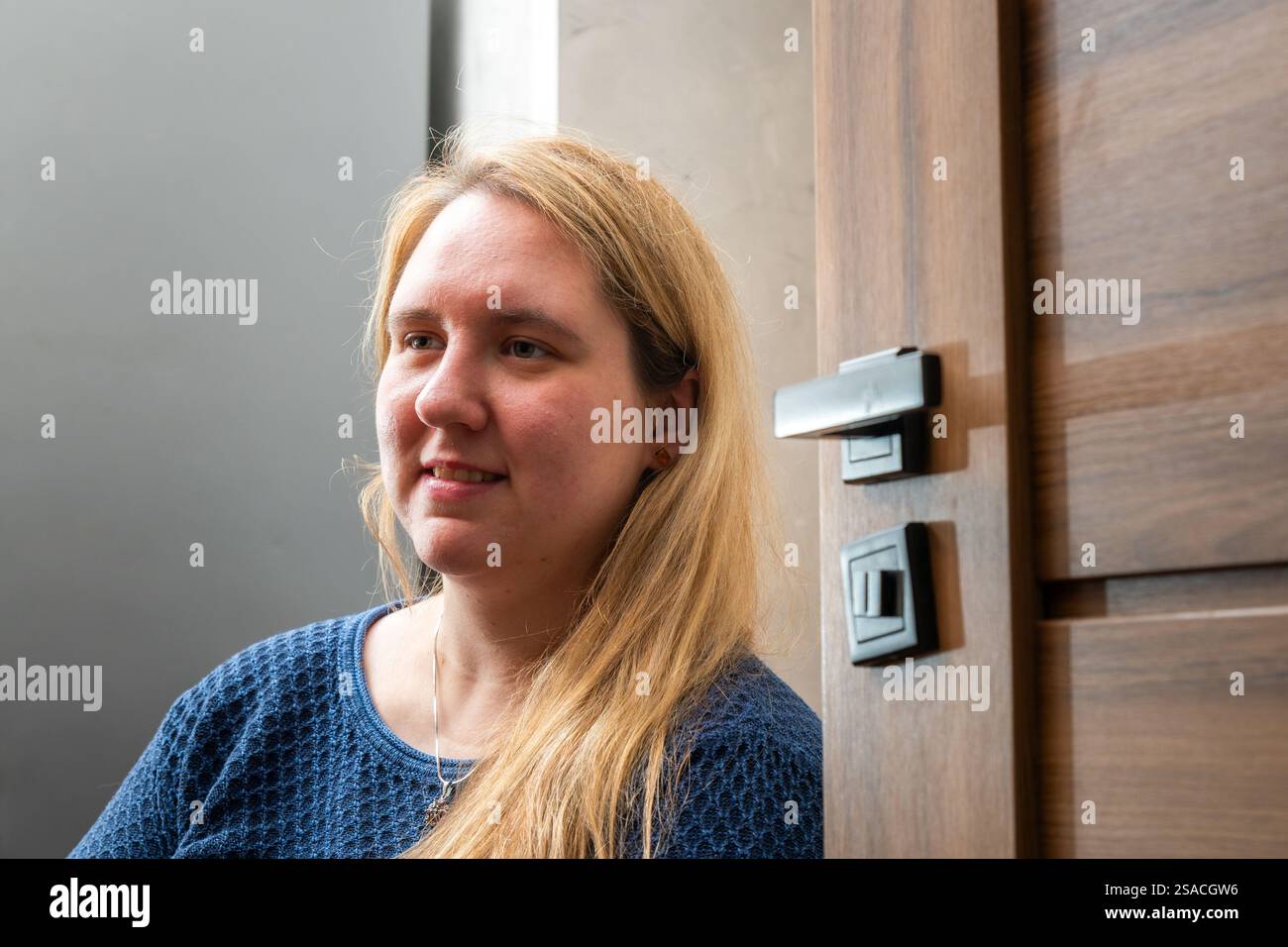 Frau mit langen Haaren, die neben einer modernen Holztür in einem Innenbereich sitzt Stockfoto