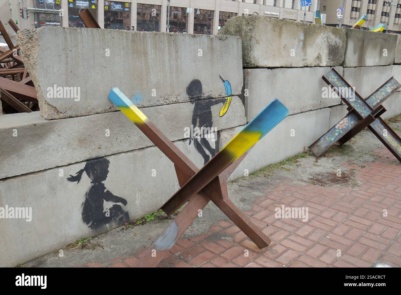KIEW, UKRAINE - 24. JANUAR 2025 - das Wandbild des in England lebenden Straßenkünstlers Banksy, das ein Panzerabwehrhindernis (tschechischer Igel) als Wippe für einen Jungen und ein Mädchen an der Kreuzung von Chreshchatyk Street und Himmlischen Hundred Heroes Alley in Kiew, Hauptstadt der Ukraine zeigt. (Foto: Eugen Kotenko/Ukrinform) Stockfoto
