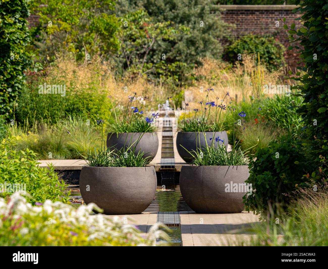 Zentraler Rang mit großen dekorativen Töpfen auf beiden Seiten im ruhigen Paradise Garden am RHS Bridgewater. Stockfoto