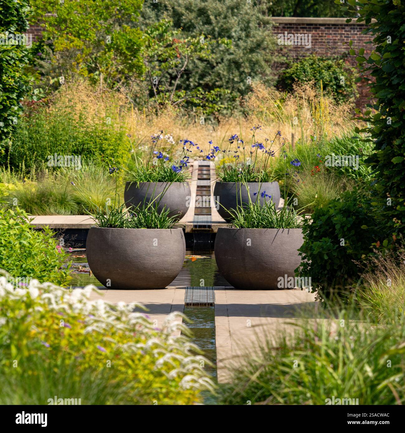 Zentraler Rang mit großen dekorativen Töpfen auf beiden Seiten im ruhigen Paradise Garden am RHS Bridgewater. Stockfoto