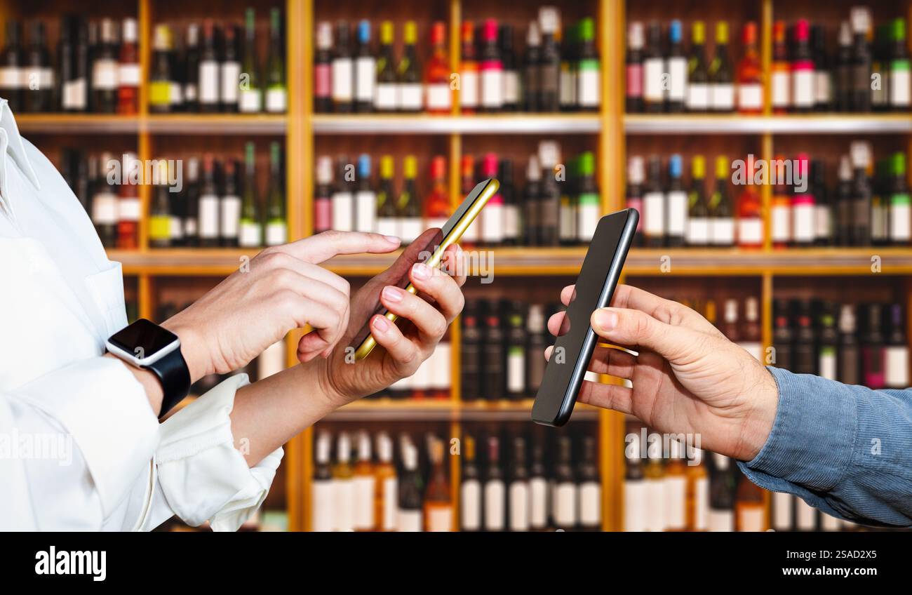 Menschen, die Smartphones vor dem Hintergrund von Weinflaschen in den Regalen im Geschäft benutzen. Mobile Zahlungstechnologien. Stockfoto