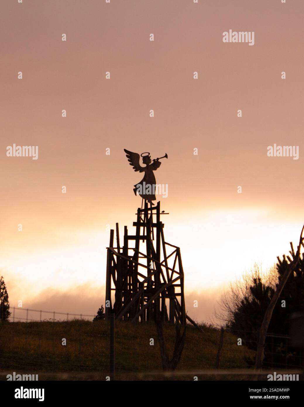 Silhouette eines Weihnachtsengels vor einem Hintergrund des Sonnenaufgangs. Weihnachtsdekoration in rustikaler Umgebung. Wintertag, bewölkter Himmel. Stockfoto