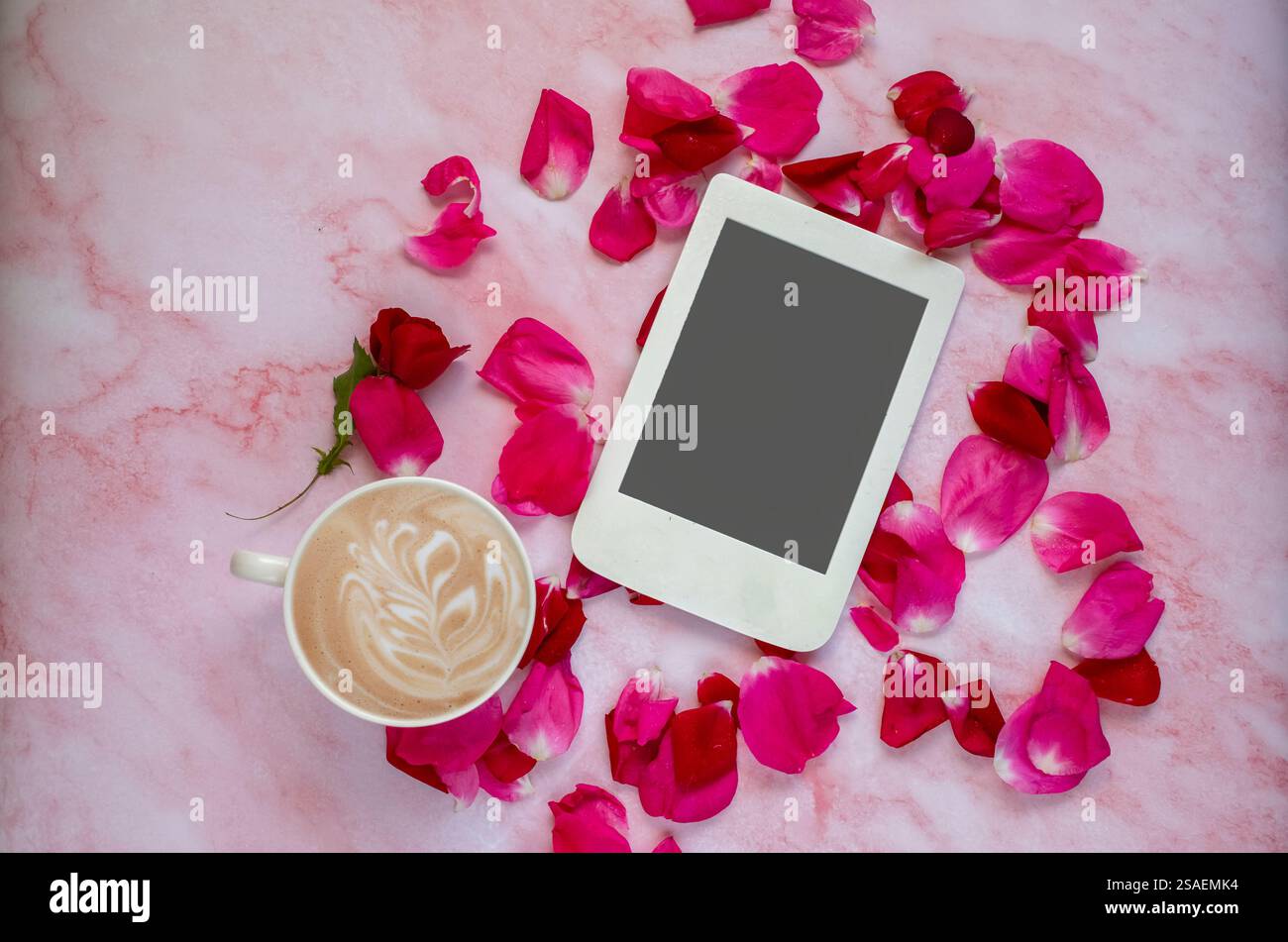 Romantische Komposition mit einer Tasse Kaffee, Rosenblättern und E-Reader mit Kopierraum auf rosa Marmorhintergrund. Vorlage für feminine Blogs. Stockfoto