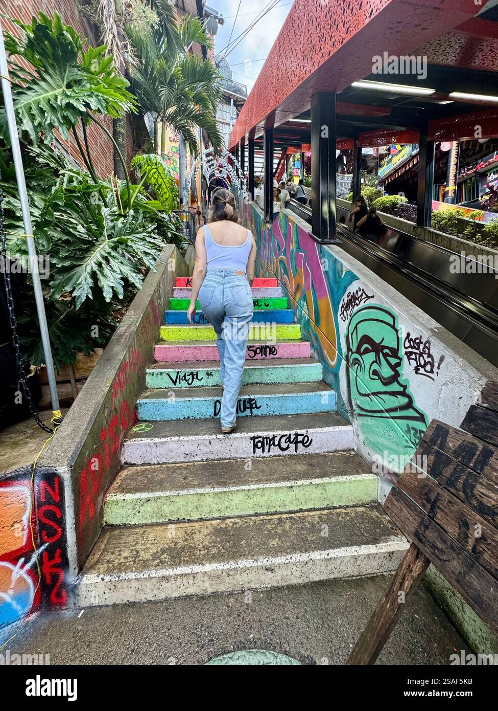Ein Mädchen, das eine Regenbogentreppe in der Comuna 13 in Medellin, Kolumbien, aufsteigt - Smartphone-aufgenommenes Stockfoto