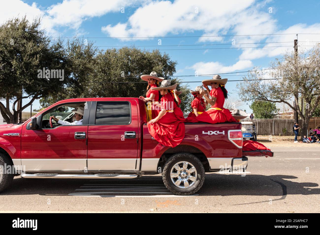 Vier Frauen in fließend roten traditionellen mexikanischen Kleidern fahren in einem Pickup-Truck bei der jährlichen Parade of Oranges, 2025, Mission, Texas, USA. Stockfoto