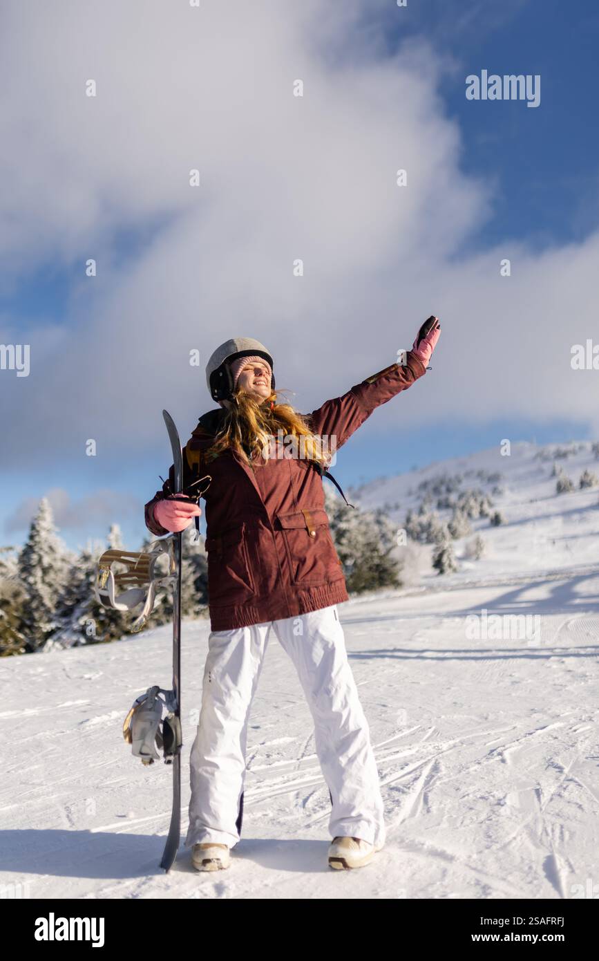 Ein Snowboarder erhebt den Arm vor Freude und steht auf einem verschneiten Berg unter einem sonnigen blauen Himmel. Wintersport, Freiheit und Outdoor-Abenteuer sind wunderschön Stockfoto