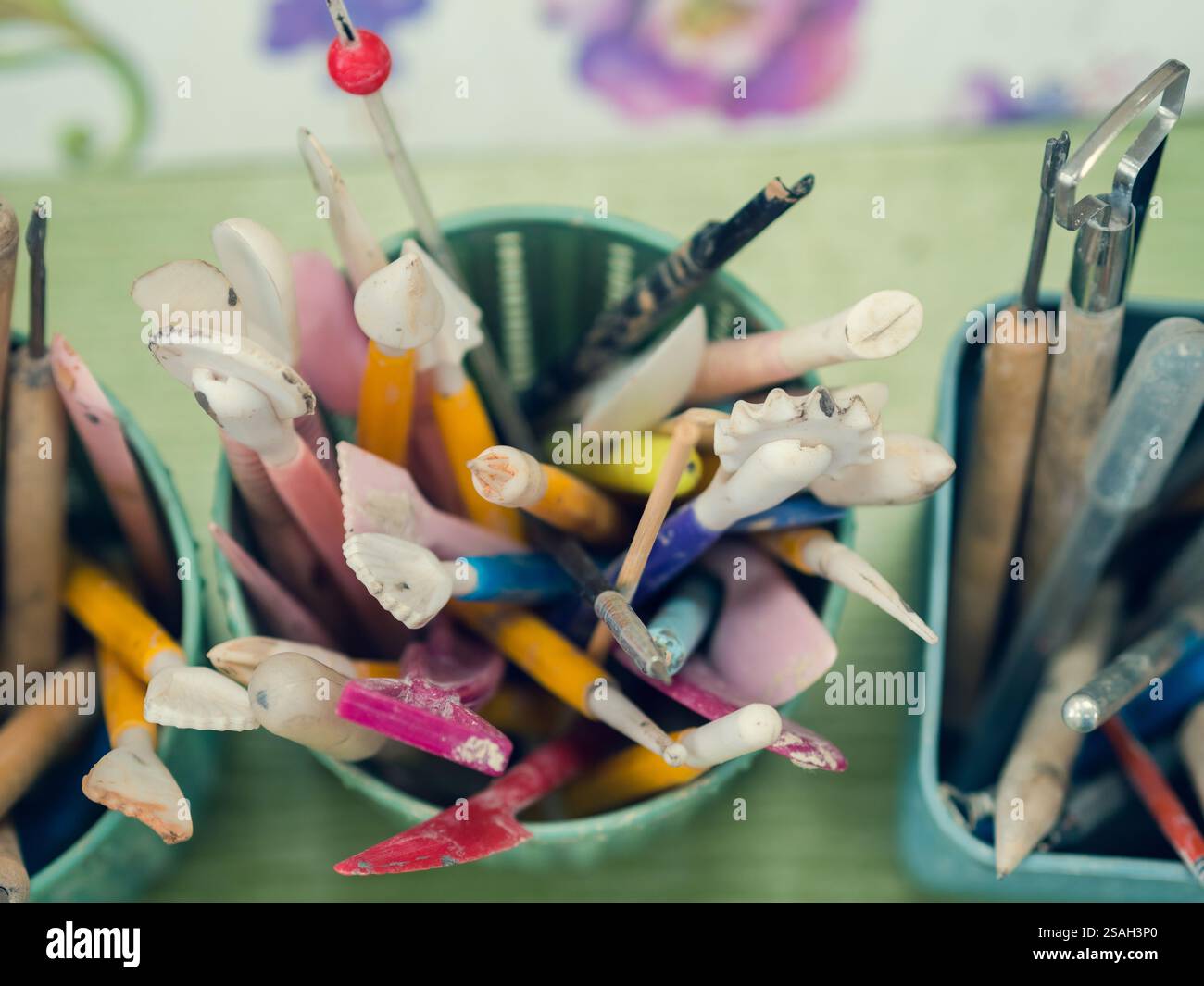Werkzeuge des Keramikkünstlers. Draufsicht auf Stapel, Jakobsmuscheln, Bleistifte und Pinsel, die sich in einem speziellen Becher befinden. Stockfoto
