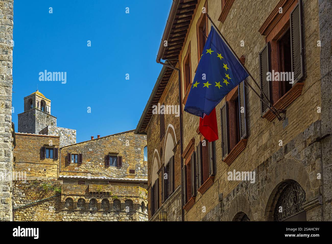 Blick auf die Häuser und Gassen der mittelalterlichen Stadt San Gimignano. Flagge der Europäischen Union. San Gimignano, Provinz Siena, Toskana, Italien Stockfoto