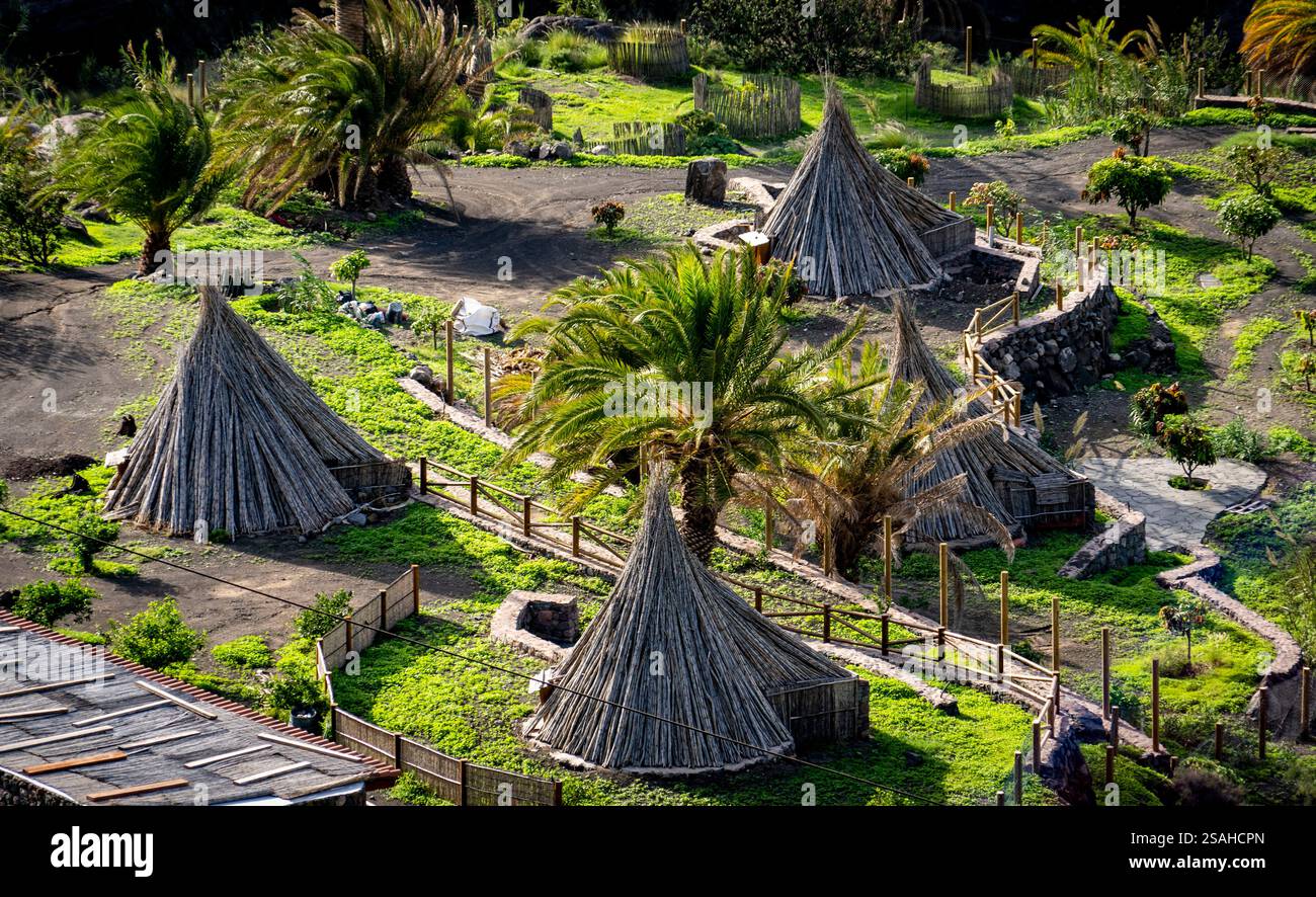 Blick aus der Vogelperspektive auf traditionelle Hütten aus natürlichen Materialien, umgeben von üppigem Grün und Palmen. Die Landschaft verfügt über Wege und Steinstraßen Stockfoto
