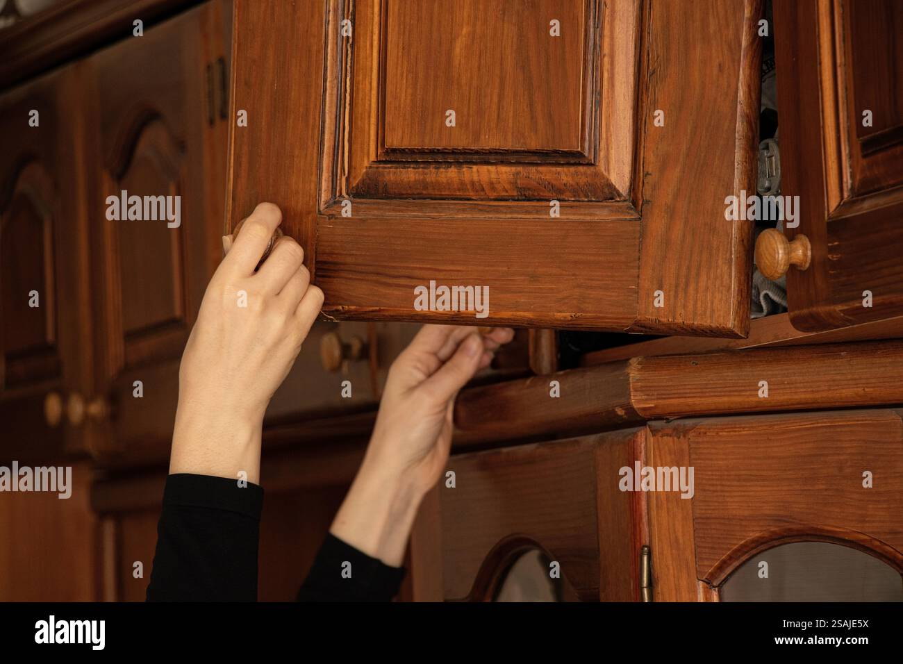 Weibliche Hand öffnet die kaputte Tür des alten Holzschranks im Schlafzimmer des Hauses, alte Möbel Stockfoto