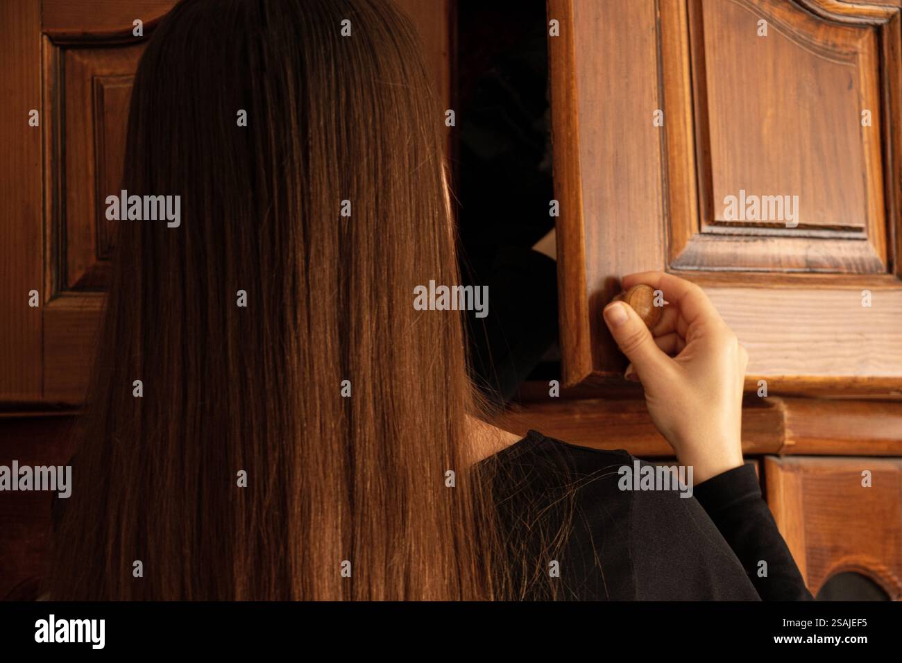 Ein Mädchen nimmt Dinge aus einem alten Holzschrank im Schlafzimmer eines Hauses, alte Möbel Stockfoto