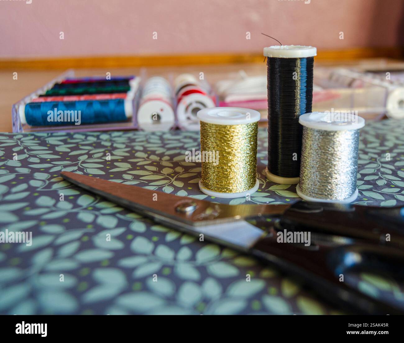 Rollen aus Metallgarn, Gold, Silber und Schwarz auf grünem floralem Hintergrund mit Schere Stockfoto