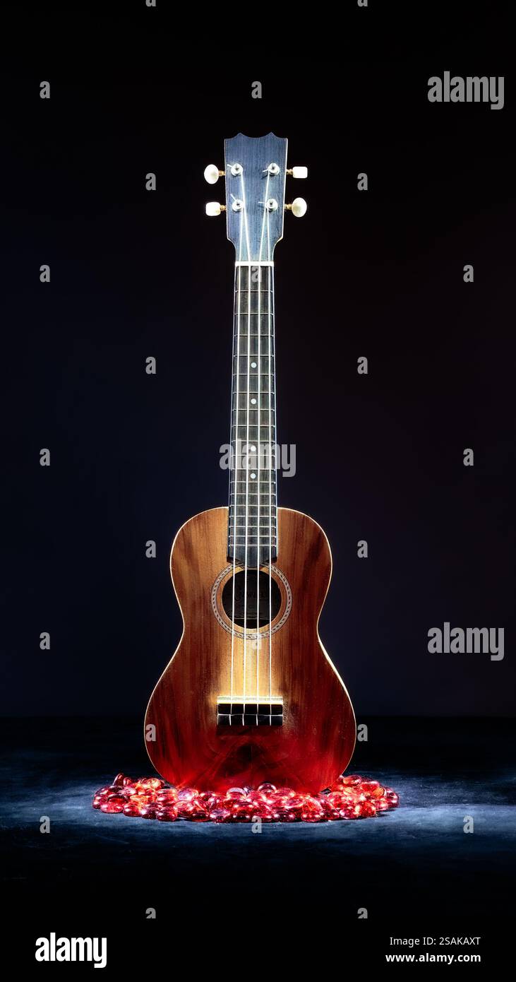Ukulele, helle Malerei im Dunkeln, brauner Hintergrund, schwarzer Vordergrund und rote Glasperlen. 2025 Stockfoto