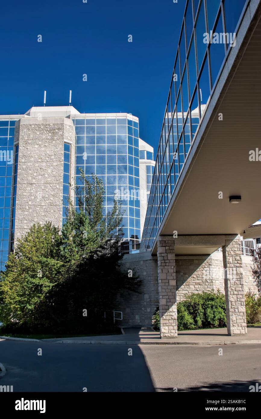 Ein großes Gebäude mit einer Glasfassade. Das Gebäude ist von Bäumen umgeben. Es gibt einen Fußweg, der zwischen dem Gebäude und den Bäumen verläuft Stockfoto