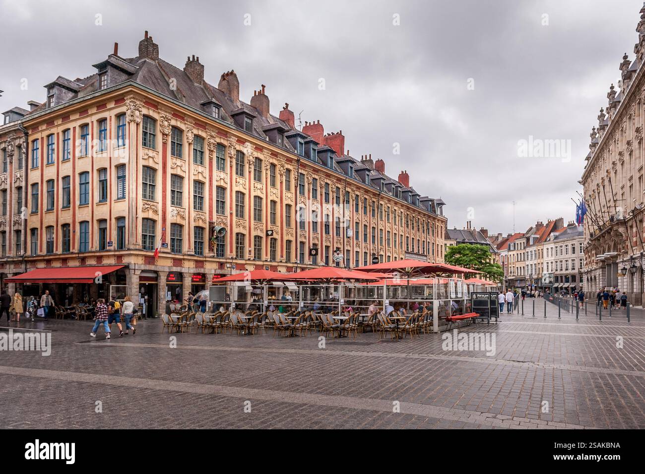 Blick auf einen historischen Platz in Lille, Frankreich, mit traditioneller flämischer Architektur, Cafés mit Terrassen und Menschen, die unter bewölktem Himmel spazieren gehen. Stockfoto