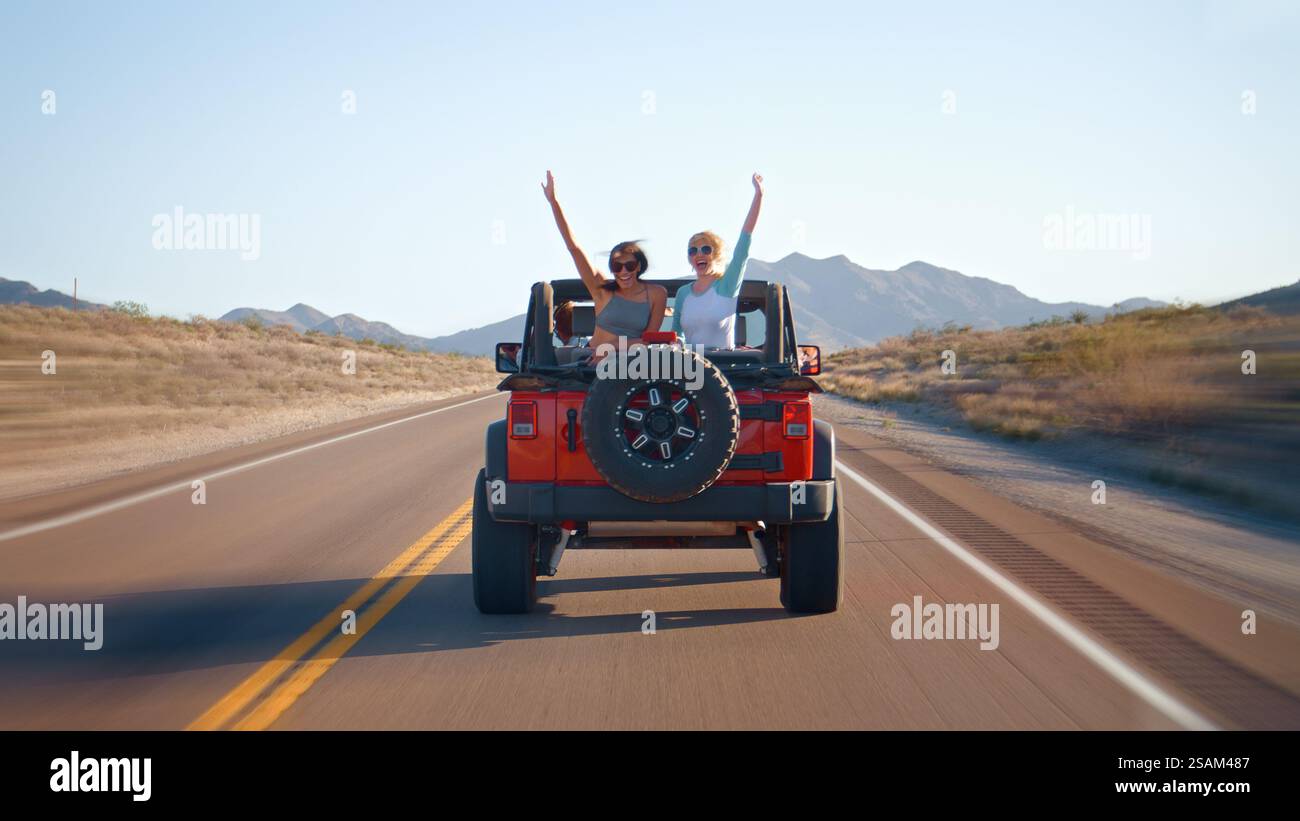 Freunde Auf Roadtrip, Die Ein Cabriolet Auf Der Landstraße Fahren, Mit Frauen, Die Hinten Winken Stockfoto